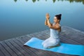 A young woman sits relaxed on a mat by the lake with her folded hands raised above her head. Meditation, yoga in nature Royalty Free Stock Photo