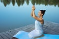 A young woman sits relaxed on a mat by the lake with her folded hands raised above her head. Meditation, yoga in nature Royalty Free Stock Photo