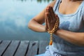 A young woman sits relaxed on a mat by the lake holding her folded hands in front of her. Meditation, yoga in nature. Close-up