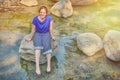 A young woman sits on a rock with her legs dangling in the water. Flooded shore with a stone bottom Royalty Free Stock Photo