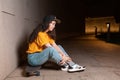 Young woman sits on a skateboard, posing on a night street. Outdoor. Side view. The concept of youth subculture Royalty Free Stock Photo