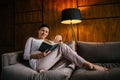 A young woman sits on a sofa with a book in her hand Royalty Free Stock Photo