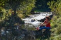 Young woman sits on a stone near a small stream on a warm autumn day