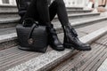 Young woman sits on stone steps outdoors in jeans in black fashion boots with a stylish leather handbag. ÃÂ¡lose-up of female legs