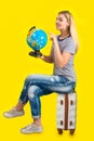 A young woman sits on a suitcase with a globe and is going on a journey. Royalty Free Stock Photo