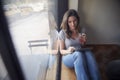 Young woman sits beside window in cafe using tablet computer Royalty Free Stock Photo