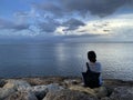 Young woman sitting alone on the beach watching the sea view. Blue sky over the ocean horizon. Tranquil nature scenery. Self love Royalty Free Stock Photo