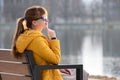 Young woman sitting alone on park bench relaxing on warm autumn day