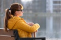 Young woman sitting alone on park bench relaxing on warm autumn day