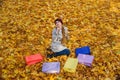 Young woman sitting on autumn leaves near colorful shopping bags. Autumn sale Royalty Free Stock Photo