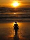 Young woman sitting on the beach, silhouette at sunset. Young woman practicing yoga outdoors. Harmony and meditation concept. Royalty Free Stock Photo