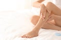 Young woman sitting on bed and applying cream onto her leg after depilation Royalty Free Stock Photo