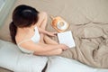 Young woman sitting in bed while reading a book with coffee cup Royalty Free Stock Photo
