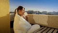 Young woman sitting behind table on the balcony and drinking coffee. People in morning, relaxing at home, enjoying city view Royalty Free Stock Photo