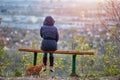 Young woman sitting on bench in autumn city park and looking at cityscape, back view Royalty Free Stock Photo