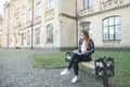 Young woman sitting on a bench on the background of a university building with a book in her hands and studying