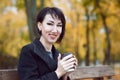 Young woman sitting on a bench and drinking coffee, autumn season, city park, yellow leaves Royalty Free Stock Photo