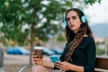 Young woman sitting on bench while listening to music with her cell phone and holding coffee cup Royalty Free Stock Photo