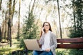Young woman sitting on bench in park talking on cell phone and using laptop. Royalty Free Stock Photo