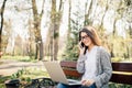 Young woman sitting on bench in park talking on cell phone and using laptop. Royalty Free Stock Photo