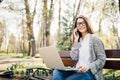 Young woman sitting on bench in park talking on cell phone and using laptop. Royalty Free Stock Photo