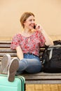 Young woman sitting on bench with suitcase talking on cellphone Royalty Free Stock Photo