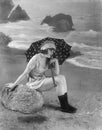 Young woman sitting on a bolder on the beach, holding an umbrella Royalty Free Stock Photo