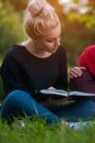 Young woman sitting with book on green lawn