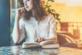 Young woman sitting in cafe at table with a paper book. Girl waiting for friends in restaurant and reading book Royalty Free Stock Photo