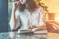 Young woman sitting in the cafe at the table with a paper book journal and looks thoughtfully out the window Royalty Free Stock Photo