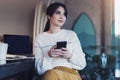 Young woman sitting cafe at table, thoughtfully looking out window, holding smartphone.Portrait girl with cell phone in her hands Royalty Free Stock Photo