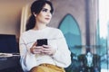 Young woman sitting cafe at table, thoughtfully looking out window, holding smartphone.Portrait girl with cell phone in her hands Royalty Free Stock Photo