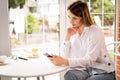 Young woman sitting in a cafe by the window with a phone waiting for a client or girlfriend. The girl is sad with a Royalty Free Stock Photo