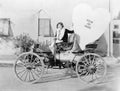 Young woman sitting on a car holding a big heart shaped sign