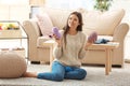 Young woman sitting on carpet and choosing tint of knitting threads indoors