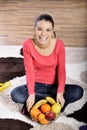 Young woman sitting on carpet and enjoying fruits