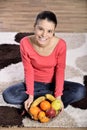 Young woman sitting on carpet and enjoying fruits