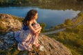 Young woman sitting on a cliff overlooking the lake, sad mood, in the evening at sunset Royalty Free Stock Photo