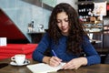 Young woman sitting at coffee shop table and writing a book Royalty Free Stock Photo