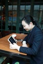 Young woman sitting in coffee shop at wooden table, drinking coffee and using pad.On table is laptop Royalty Free Stock Photo