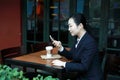 Young woman sitting in coffee shop at wooden table, drinking coffee and using smartphone.On table is laptop Royalty Free Stock Photo