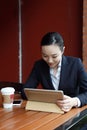 Young woman sitting in coffee shop at wooden table, drinking coffee and using pad.On table is laptop Royalty Free Stock Photo