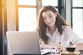 Young woman sitting in coffee shop at wooden table, drinking coffee and using smartphone.On table is laptop for internet shopping Royalty Free Stock Photo