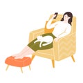 Young woman sitting in comfy yellow chair with footrest, using smartphone. Stay home concept. Girl with a white cat Royalty Free Stock Photo