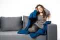Young woman sitting on a couch, holding her head, having a strong headache covered blanket Royalty Free Stock Photo