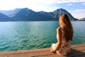 Young woman sitting on a deck by the water, looking into the distance. Carefree bright future concept. Back view beautiful woman Royalty Free Stock Photo