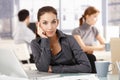 Young woman sitting at desk others working behind Royalty Free Stock Photo