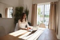 Young woman sitting at desk and working on laptop remotely. Freelancer, entrepreneur. Woman sitting at home on daytime Royalty Free Stock Photo