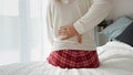 Young woman sitting on the edge of the bed in pajamas, rubbing her aching back. A concept of health problems, pain management, and Royalty Free Stock Photo