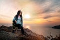 A young woman sitting on the edge of a cliff. In the background, the sea and the sky at sunset.Copy space. Concept of Hiking and